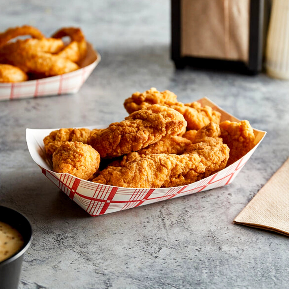 A paper-lined tray of golden fried chicken tenders on a gray tabletop, with a dipping sauce cup nearby.