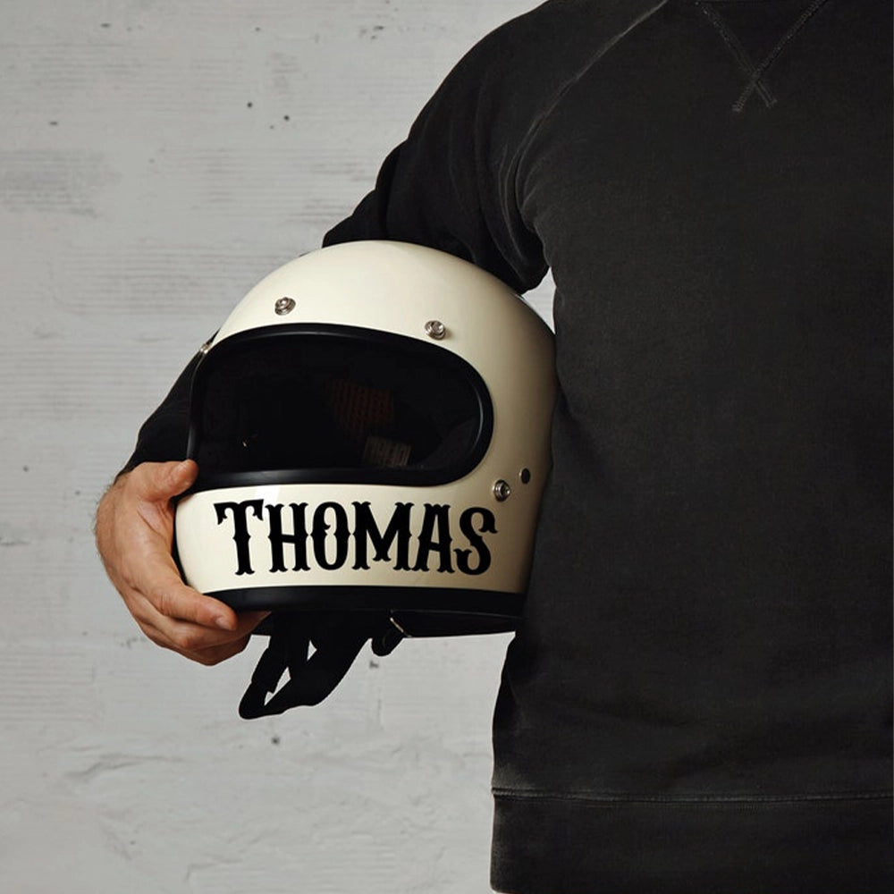 A person holding a white motorcycle helmet with the name 'THOMAS' printed on the front.