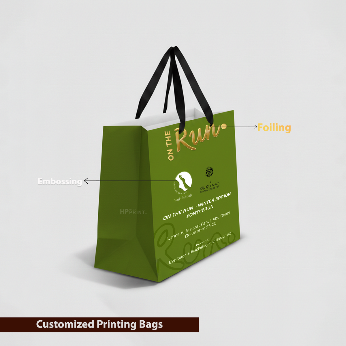 Green paper gift bag with gold text and black handles on a light gray background