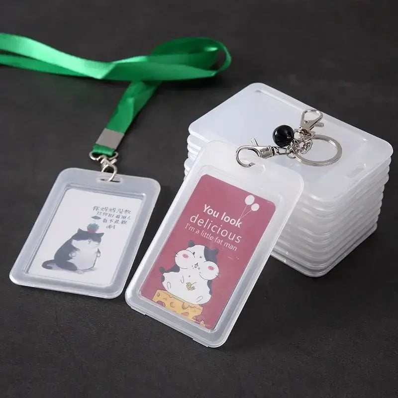Clear plastic ID badge holders with a green lanyard and keyring clips, shown with illustrated cards inside and a stack of empty holders on a dark surface.