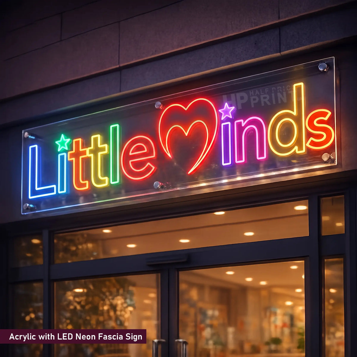 A colorful acrylic LED neon-style sign mounted above a storefront window, displaying the words "Little minds" with a heart and stars in rainbow colors. The sign is shown installed on a building exterior at night.