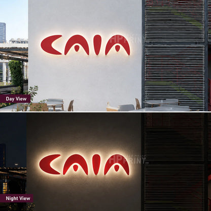 A split view showing a red illuminated backlit sign with the word CAIA in stylized lettering, labeled Day View on the top and Night View on the bottom. The top half shows the sign lit against a light wall during daytime, and the bottom half shows it lit against a darker exterior wall at night.
