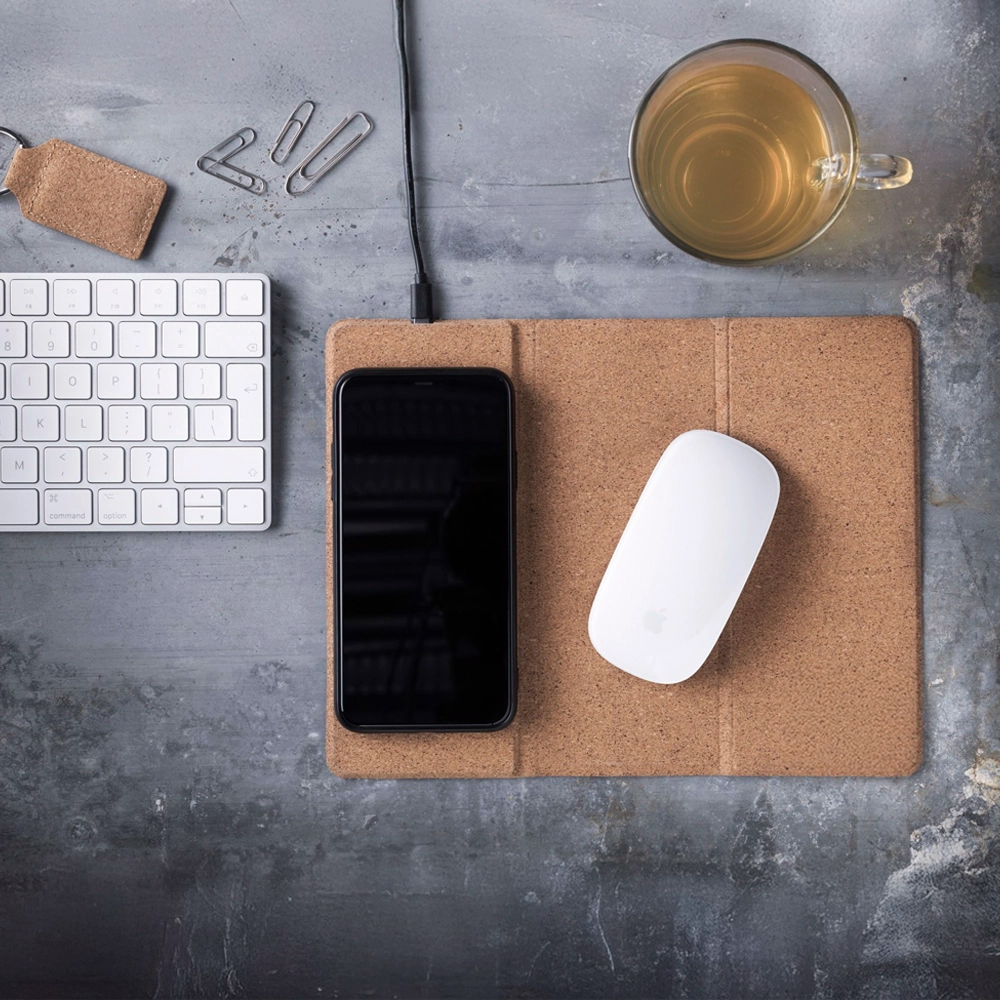 Desk setup with phone, mouse, keyboard, and cup of tea on a gray surface