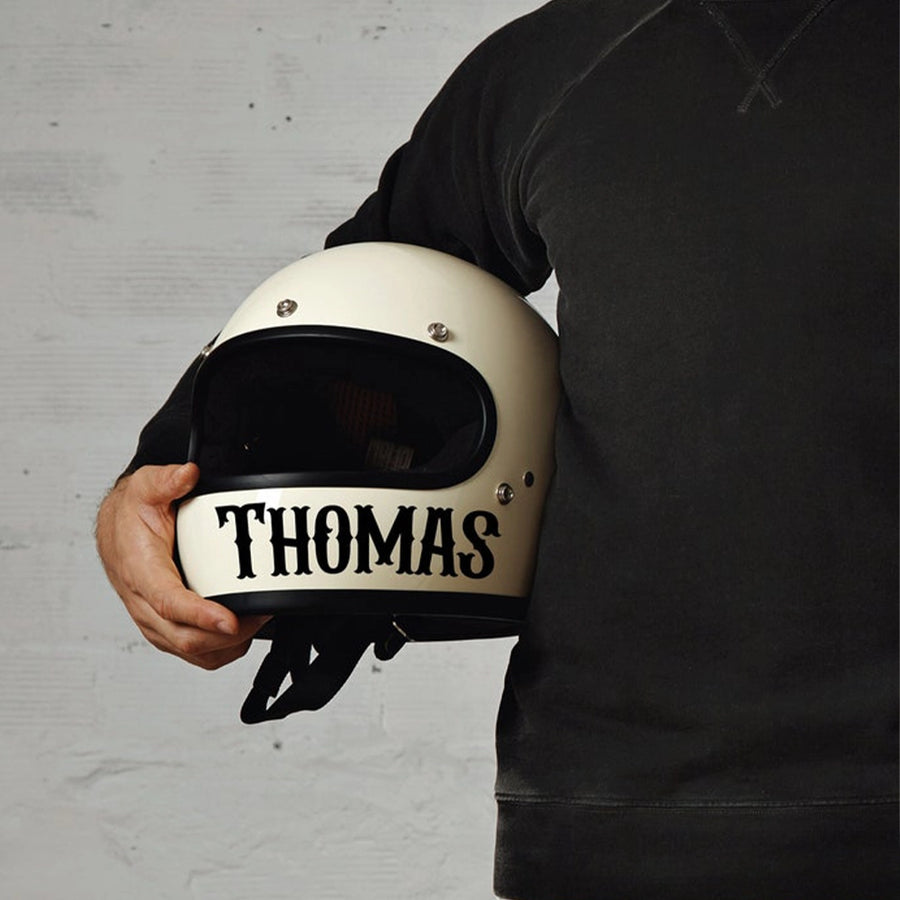 A person holding a white motorcycle helmet with the name 'THOMAS' printed on the front.