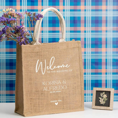 A brown jute bag with white text printed on it, featuring a cotton handle and a floral design in the background.