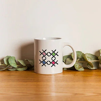 White ceramic mug with geometric print on wooden surface, greenery in background