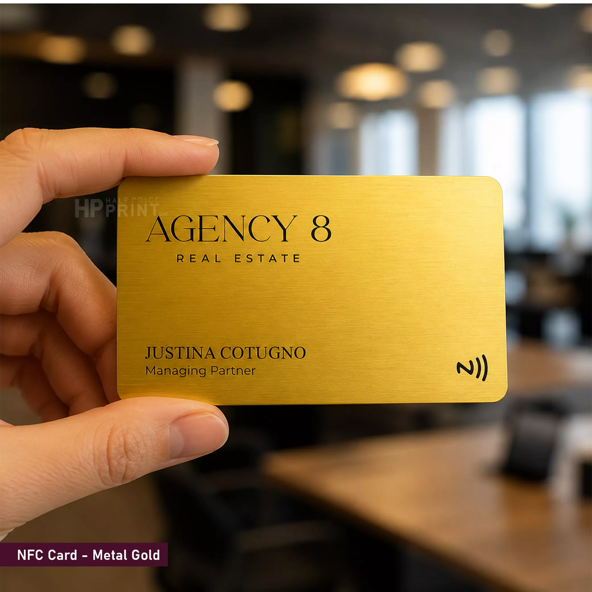 A hand holds a metallic gold real estate NFC card labeled 'Agency 8 Real Estate' and 'Justina Cotugno Managing Partner' against a blurred office background.