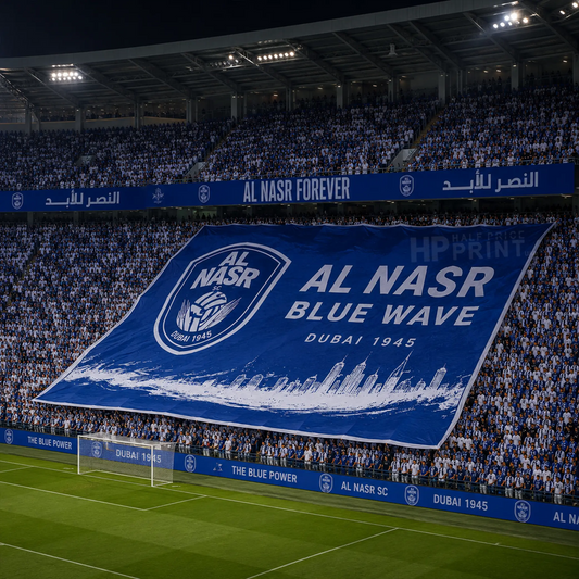 A large blue and white Al Nasr FC banner reading 'AL NASR BLUE WAVE DUBAI 1945' is held up in a stadium filled with fans. The scene is taken at night under stadium lights, with the green soccer field visible in the foreground and advertising boards around the stands.