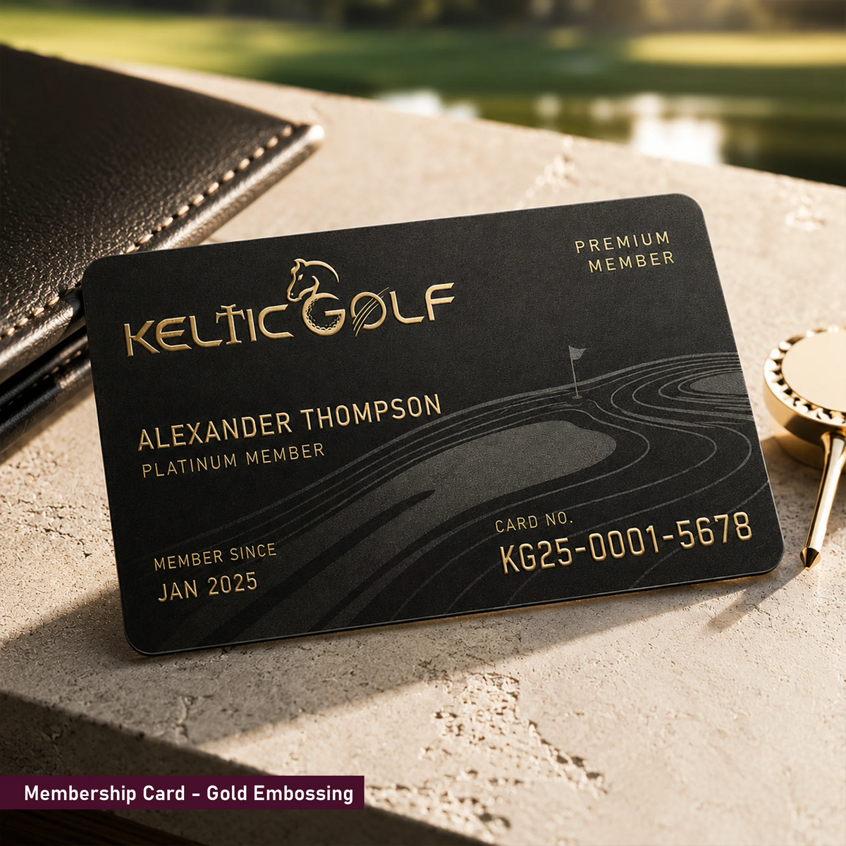 A black Keltic Golf premium membership card with gold lettering and engraved golf-course line art, resting on a stone surface beside a leather wallet and a gold keyring.