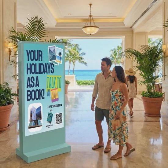 Digital totem display in a resort lobby showing a holiday booking advertisement with a couple walking past.