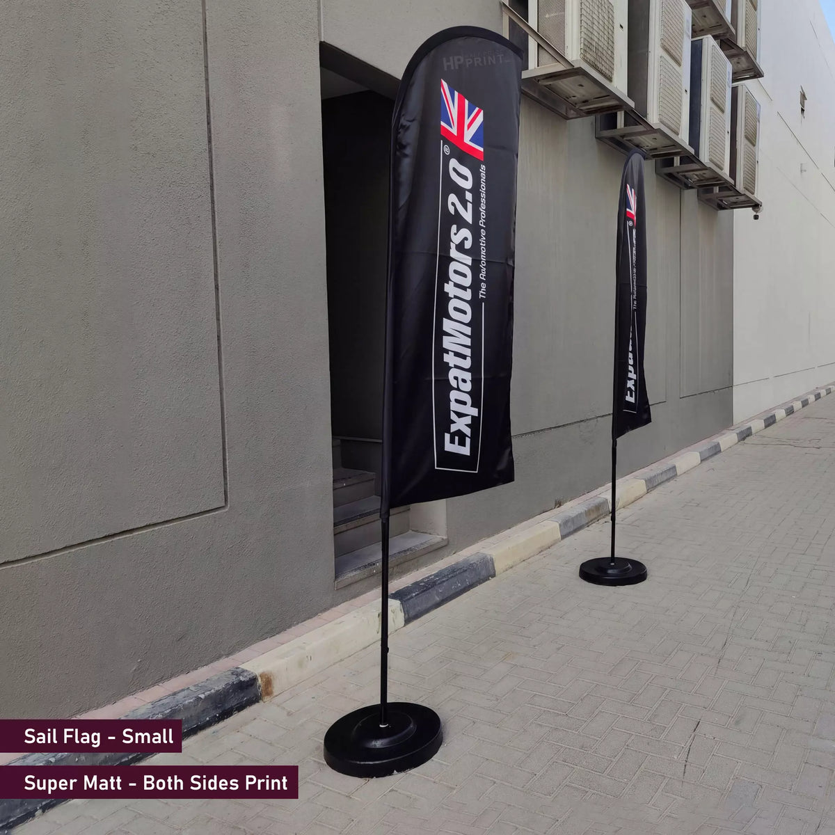 Two black flags with branding on a sidewalk next to a building.