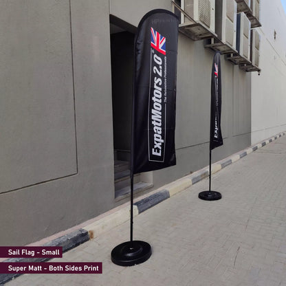 Two black flags with branding on a sidewalk next to a building.