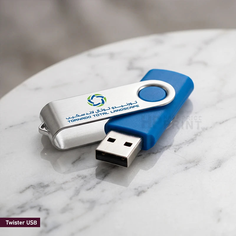 A custom branded Twister USB flash drive with a blue and silver swivel design, resting on a white marble surface. The silver section features a green and blue logo and the text 'TOWNHOOD TOTAL LANDSCAPE'.