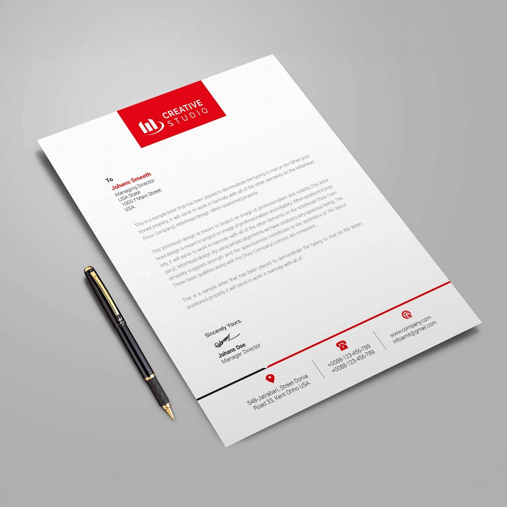 Clean, modern creative studio letterhead with a red logo and neatly formatted text, shown at an angle on a gray surface with a black pen beside it.